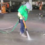 Blasting contractor using a silent blast nozzle in parking garage with blasting skid in background